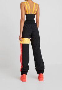 Svart och gul träningsoutfit med en åtsittande topp med dubbla axelband och lösa byxor med röd och gul färgblockering.