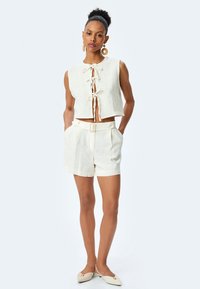 Top in lino corto con lacci davanti, abbinato a pantaloni shorts a vita alta. Entrambi in bianco sporco, con vita regolabile e vestibilità comoda.