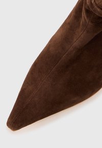 Brun mockaskinnspetsig stövel med en slät textur. Har en sömlös design och en smal, avsmalnande silhuett.