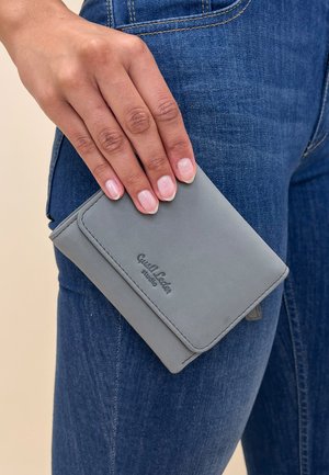 Gray leather wallet held against denim with visible stitching and embossed logo, featuring a rectangular shape and soft texture.