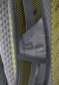 Material de mochila gris con acentos de malla, con un revestimiento interior amarillo. Logo de "Jack Wolfskin" visible en un parche gris texturizado.