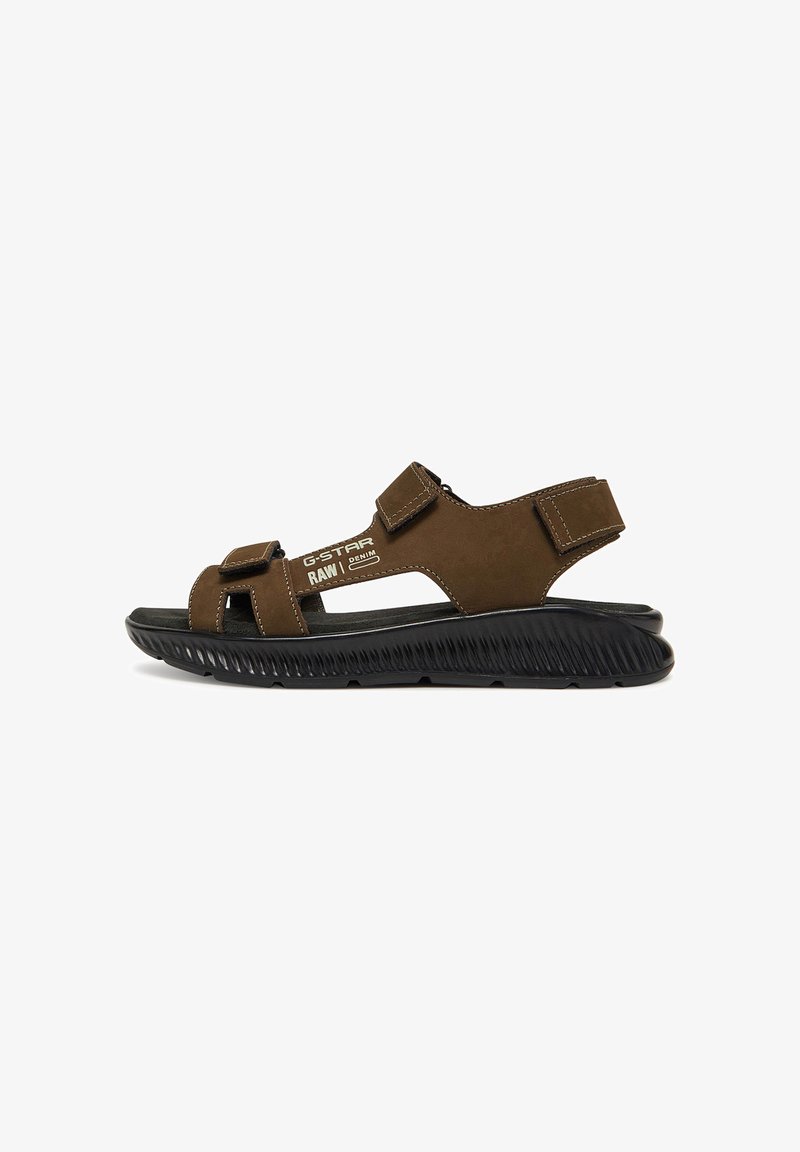 Brown leather sandal with open toe, adjustable Velcro straps, a cushioned black rubber sole, and textured detailing along the sole.