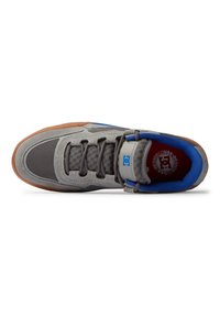Grijze sneaker met bovenwerk van mesh en suede, blauwe accenten, bruine rubberen zool en grijze veters. Merklabel zichtbaar aan de binnenkant.