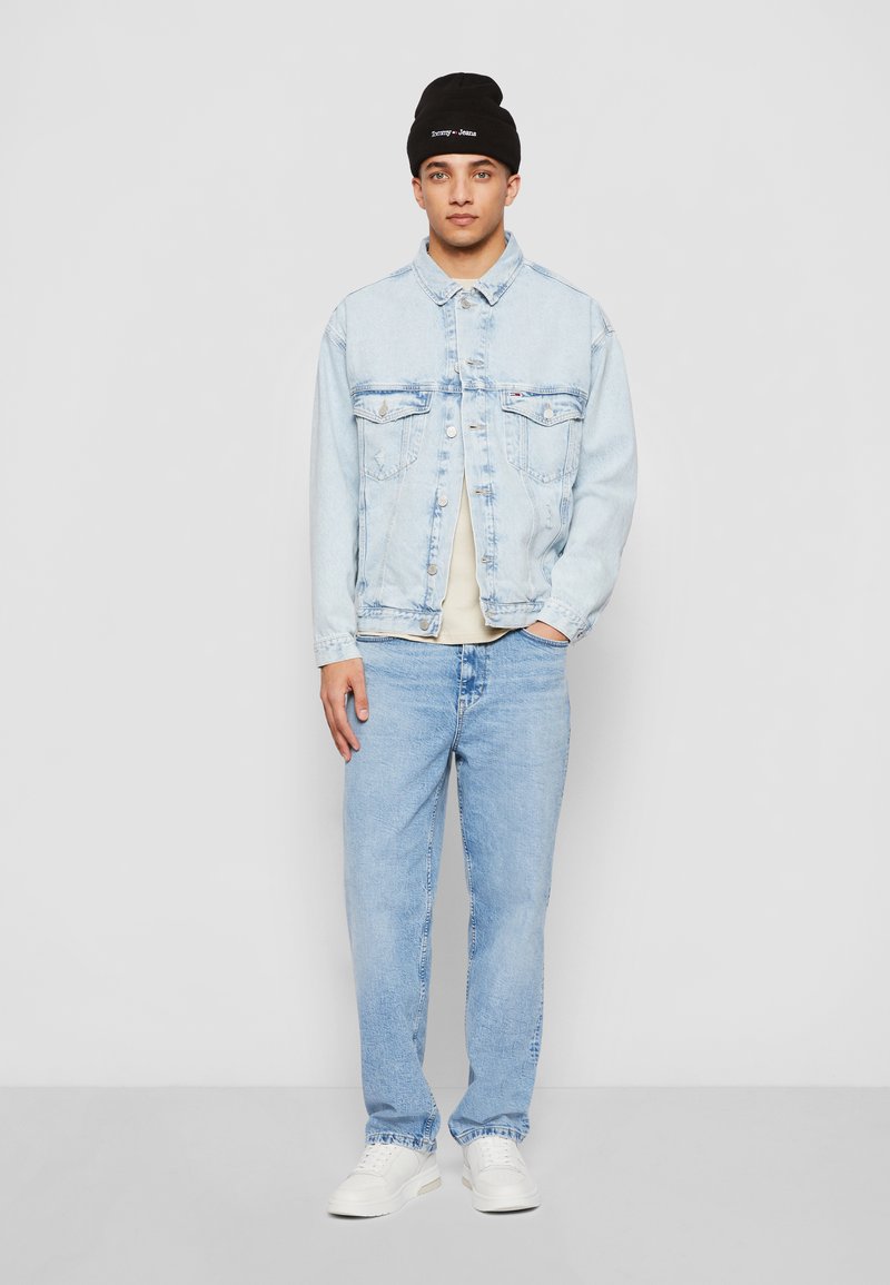 Jasnoniebieska dżinsowa kurtka z kieszeniami na piersi, kremowa koszulka pod spodem, jasnoniebieskie dżinsy i czarna czapka beanie. Białe trampki dopełniają strój.