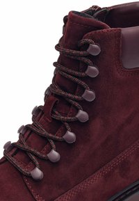 Cizme din suede burgundy cu finisaj texturat, dotate cu șireturi împletite, ochiuri din plastic și guler căptușit pentru confort și suport.