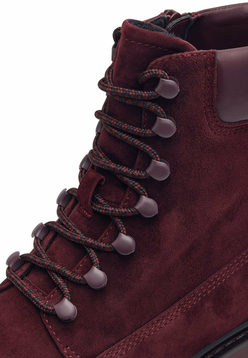 Stivale in suede bordeaux con finitura testurizzata, dotato di lacci intrecciati, passanti in plastica e uno scollo imbottito per comfort e supporto.