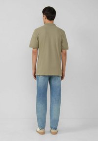 Olivgrünes Poloshirt mit kurzen Ärmeln, kombiniert mit hellblauen geraden Jeans. Das Outfit zeichnet sich durch ein minimalistisches Design und eine lässige Passform aus.