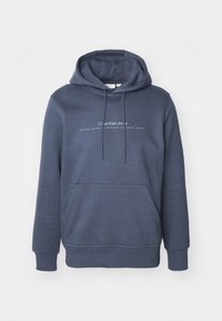 Navyblauwe katoenen hoodie met een voorke pocket, een capuchon met trekkoord en een grafische tekst "Calvin Klein Jeans" op de borst. Gladde textuur.