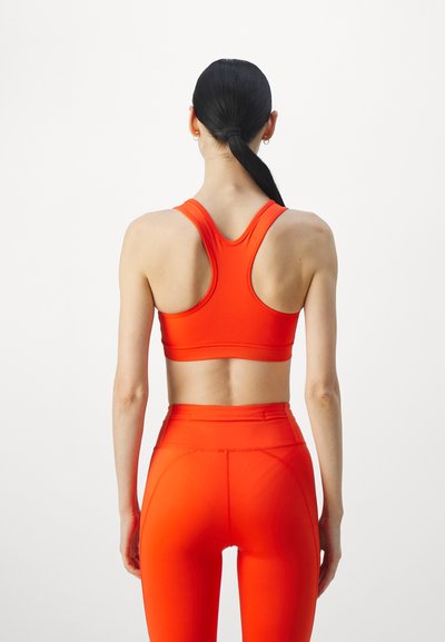 Red sports bra with a racerback design paired with high-waisted leggings, both made from a smooth, stretchy material.