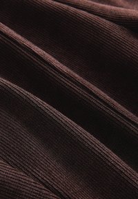 Mørkebrunt ribbet stof med bløde folder, der danner diagonale linjer og teksturerede skygger på tværs af overfladen.