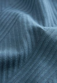 Textureret stof i dæmpet blå med diagonale striber, der har et strikket mønster, som skaber en subtil dybde og varieret overfladefornemmelse.
