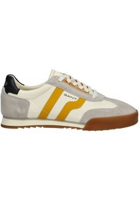 Sneaker con tomaia crema, accenti in suede grigio, strisce gialle, tallone nero e suola in gomma marrone; presenta lacci bianchi e marchio.