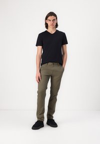 Černé tričko s výstřihem do V, olivově zelené slim-fit kalhoty, černé tenisky. Jednoduchý design, bavlněný materiál, přiléhavý střih, minimální kovové detaily.