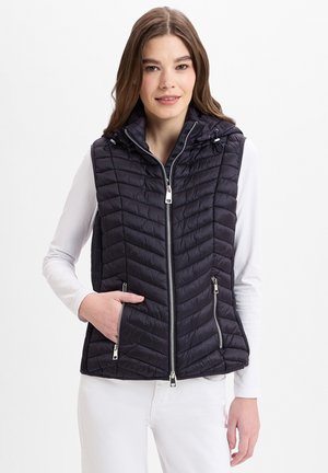 Schwarze Steppweste mit einem gesteppten Design, Reißverschluss vorne, seitlichen Taschen und einer Kapuze, getragen über einem langärmeligen weißen Oberteil. Glatte Textur.