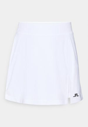 White tennis skirt with a smooth, lightweight fabric, featuring a side slit and a black logo accent on the lower left hem.