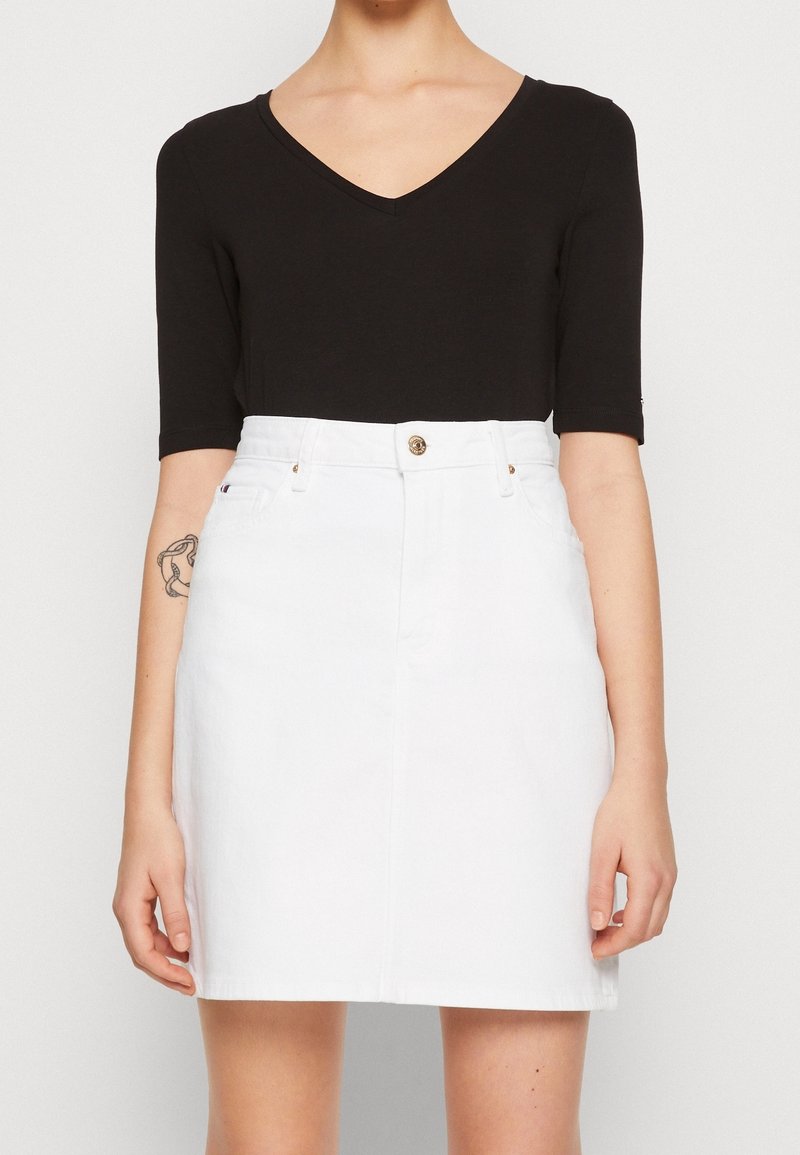 Top negro de manga corta con escote en V, combinado con una falda de mezclilla blanca que presenta un cierre frontal de botones y detalles de costura sutiles.