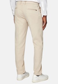 Beige bikses ar šauru piegriezumu, ar rāvējspiedni aizmugures kabatā, valkātas ar baltām kedām. Audumam ir gluda tekstūra.