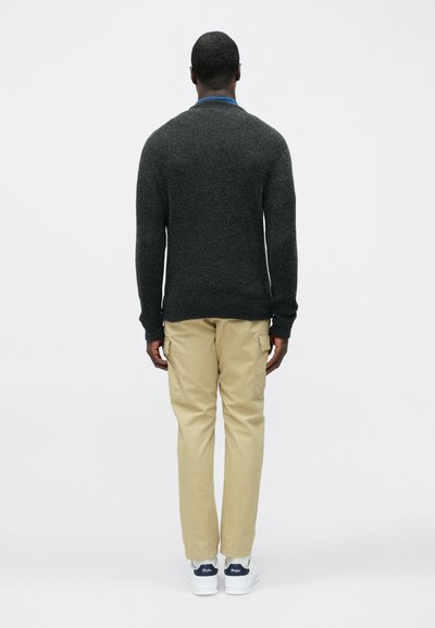 Temno sivi pleteni pulover z okrolim izrezom, kombiniran z bež cargo hlačami in belimi supergami, prikazan od zadaj na enostavni podlagi.