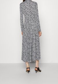 Frau in einem langärmligen, schwarz-weißen Zebradrücken-Midikleid mit schwarzen Slingback-Absatzschuhen, die vor einem schlichten Hintergrund steht.