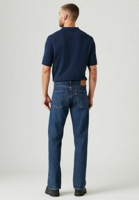Dunkelblaues Poloshirt mit kurzen Ärmeln, kombiniert mit geraden dunkelblauen Jeans aus Denim, die mit einem Lederaufnäher und auffälliger Rückentaschennaht versehen sind.
