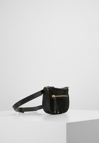 Musta käsilaukku, jossa on pyöristetty muoto, valmistettu nahasta ja mokkanahasta. Siinä on kullanväriset metalliosat, vetoketjullinen suljin ja säädettävä olkahihna.