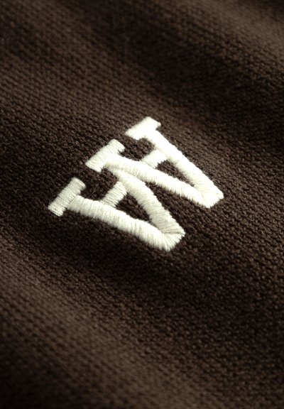Una tela marrón con una textura suave presenta un destacado logo bordado en blanco, que muestra un diseño estilizado de "AW".