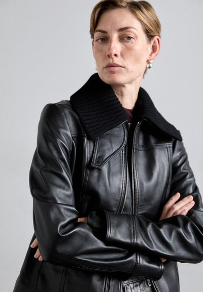 Black leather jacket with a ribbed black collar, zip closure, and tailored fit, highlighting smooth texture and minimalist design.