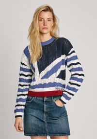 Pull en tricot de couleur bleu marine, blanc et bleu avec un motif rayé et un ourlet côtelé rouge. Associé à une jupe en denim. Conception en dentelle complexe.