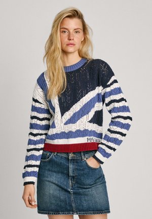Pull en tricot de couleur bleu marine, blanc et bleu avec un motif rayé et un ourlet côtelé rouge. Associé à une jupe en denim. Conception en dentelle complexe.