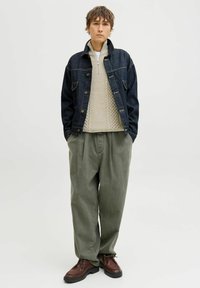 Veste en denim, pull en maille beige, pantalon ample vert olive et chaussures à lacets marron. Les caractéristiques comprennent des coutures visibles et des détails de poches.