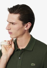 Polo shirt verde scuro con un tessuto testurizzato, pattina con due bottoni e un piccolo logo di coccodrillo ricamato sul lato sinistro del petto.