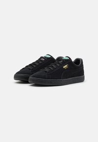 Schwarze Wildledersneaker mit einer strukturierten Gummisohle, flachen Schnürsenkeln und goldener Branding. Besitzt einen gepolsterten Schaft und kontrastierende Zungenakzente.