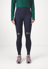 Mornarice športne leggice iz elastičnega materiala z zlatim logotipom Adidas in grafiko maratona, z visoko pasom in gladko teksturo.