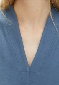 Vaaleansininen vaate, jossa on syvä V-muotoinen kaula-aukko ja siistit ompelu yksityiskohdat. Sujuva rakenne, kangas näyttää kevyeltä ja hengittävältä.