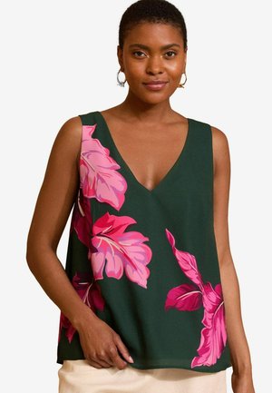 Top de tirantes verde con patrones de hojas grandes en rosa, diseño de escote en V profundo y textura de tela suave. Modelo vistiendo pantalones en colores neutros.