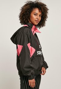 Zwarte en roze windbreaker jas met een ritssluiting aan de voorkant, elastische manchetten en een cinched onderkant. Kenmerkt zich door een logo op de borst. Gestructureerde stof.