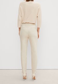Pantaloni fitted beige con una texture liscia e un design slim. Il retro presenta due tasche. Indossati con un morbido maglione beige e tacchi beige.