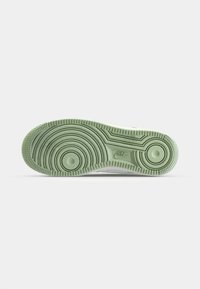 Zielona gumowa podeszwa z zaokrąglonymi rowkami, okrągłymi wzorami i teksturowanym uchwytem. Posiada logo Nike w pobliżu obszaru pięty.