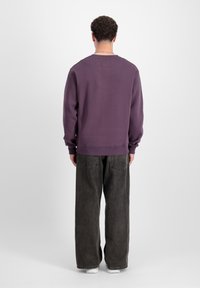Lilla bomuldssweatshirt med rund hals, ribbede ærmer og kant, parret med oversized mørkegrå jeans. Ensfarvet baggrund.