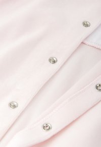 Tejido de color rosa claro con una textura suave, que cuenta con broches de presión plateados a lo largo del borde y un forro interior liso.