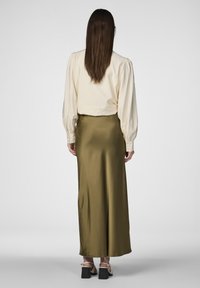 Blouse créme �à manches bouffantes avec un cropped associée à une longue jupe satin olive, et des sandales à talons carrés noires.
