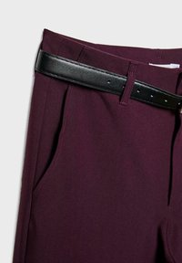 Gros plan sur un pantalon violet foncé avec poche latérale et ceinture en cuir noir passée dans les passants de ceinture.