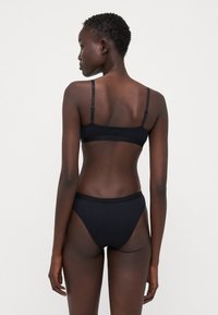 Svart undertøysett med en sømløs bralette med tynne justerbare stropper og matchende høyhåndte undertøy, begge i et glatt, mykt materiale.