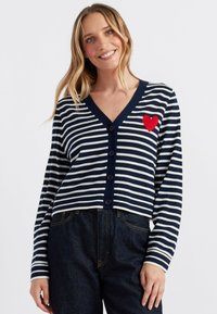 Cardigan a righe blu e bianche realizzato in tessuto morbido, con scollatura a V, bottoni frontali e una patch a forma di cuore rosso sul petto sinistro.