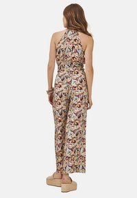 Chándal floral multicolor con cuello halter, cintura elástica y piernas anchas. Tejido ligero con textura suave. Sandalias de plataforma puestas.