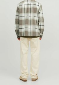 Camicia a quadri in flanella grigia e bianca, con orlo posteriore allungato, abbinata a pantaloni dritti color crema e scarpe beige.