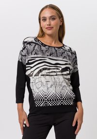 Schwarzes und weißes Langarmoberteil mit einem strukturierten Grafikmuster aus Punkten, Streifen und abstrakten Designs, hergestellt aus einem weichen Stoff.