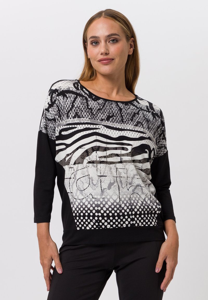 Schwarzes und weißes Langarmoberteil mit einem strukturierten Grafikmuster aus Punkten, Streifen und abstrakten Designs, hergestellt aus einem weichen Stoff.