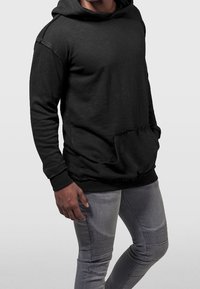 Sudadera con capucha negra y bolsillo frontal, con tejido texturizado y un ajuste relajado, combinada con jeans ajustados gris claro con detalles acanalados.