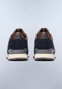 Sneaker in suede blu navy con dettagli in pelle marrone, dotate di un logo sul tallone e una suola in gomma texturizzata beige e grigia.